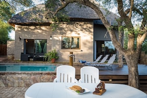 A modern house with a pool, white chairs, and a dining table with food. - Nkanyi Wildlife House & Cottage (Hoedspruit)