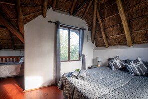 Una habitación con una cama, ventana, techo de madera y mesita de noche.