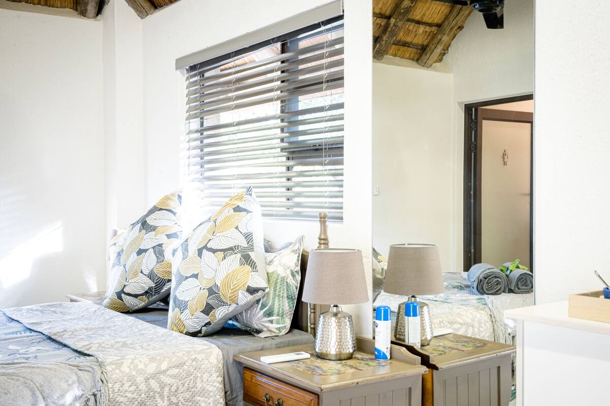A neatly arranged hotel room with a bed, bedside tables, a lamp, and a window with blinds.