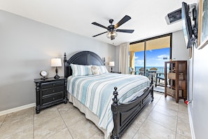 A bedroom with a bed, nightstands, a ceiling fan, and a view of the outdoors.