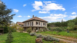 Une maison à deux étages avec une grande pelouse devant, un chemin menant à l’entrée et un jardin agrémenté d’arbustes et d’un rocher.