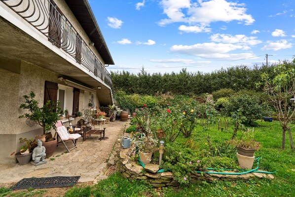 A house with a stone patio, outdoor furniture, and a garden with various plants and flowers.