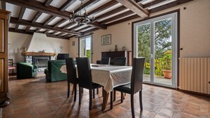 Un coin repas avec une table dressée pour quatre personnes, une cheminée et une vue sur un jardin extérieur, visible à travers une porte vitrée.