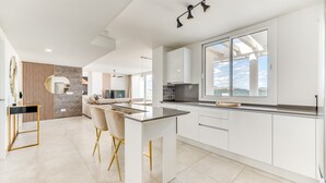 Una cocina moderna con una isla grande, armarios blancos y vistas al mar.