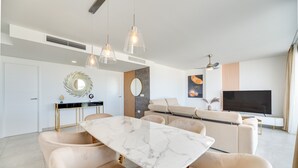 Un espacio moderno para vivir con una mesa de comedor de mármol, sofás color beige, un televisor e iluminación colgante.