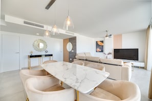 Un espacio moderno para vivir con una mesa de comedor de mármol, sofás color beige, un televisor e iluminación colgante.