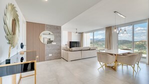 Una sala de estar moderna con un sofá, una mesa de comedor y ventanas amplias que ofrecen una vista.