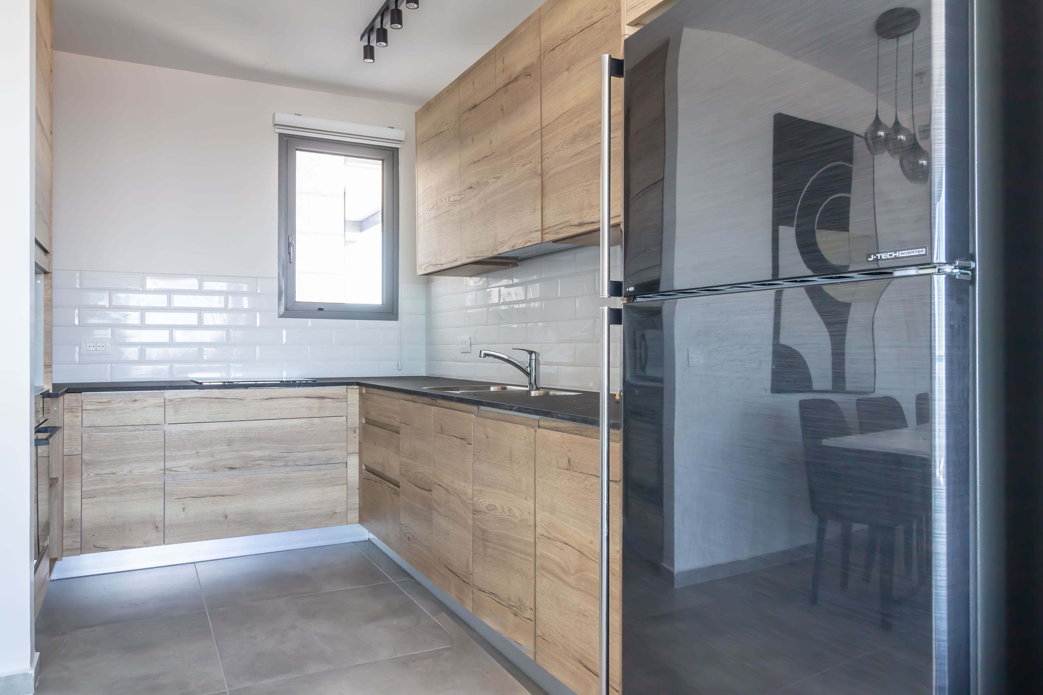 A modern kitchen with wooden cabinets, a stainless steel refrigerator, and a window providing natural light.