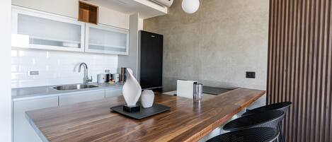A modern kitchen with a wooden countertop, white cabinets, and black chairs.