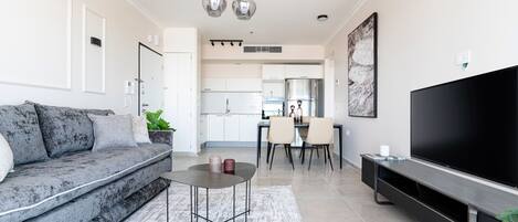 A modern living room with a grey sofa, a coffee table, a TV stand, and a dining area with chairs and a table.