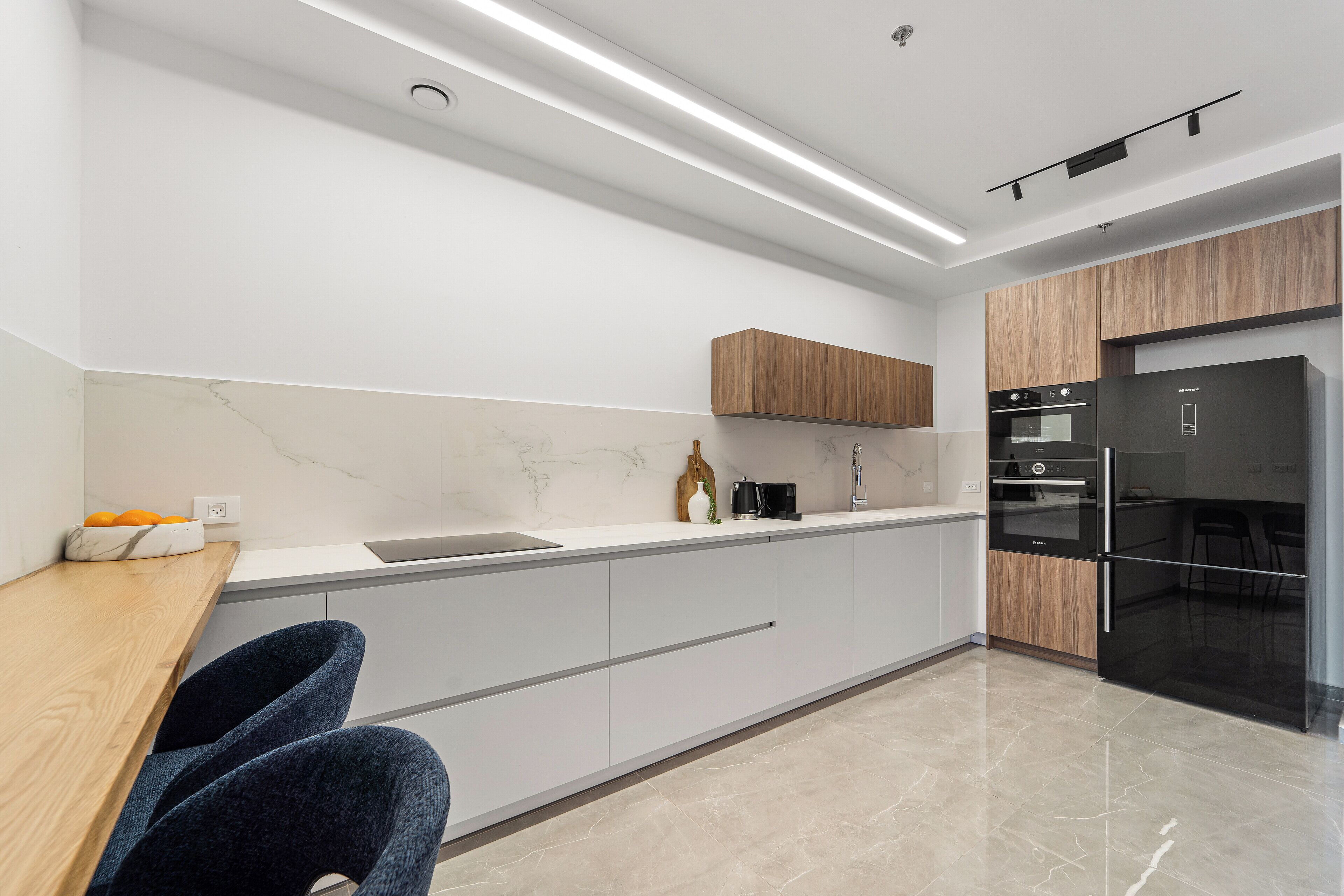 Une cuisine moderne dotée d’un plan de travail en marbre, de meubles en bois et d’un réfrigérateur noir.