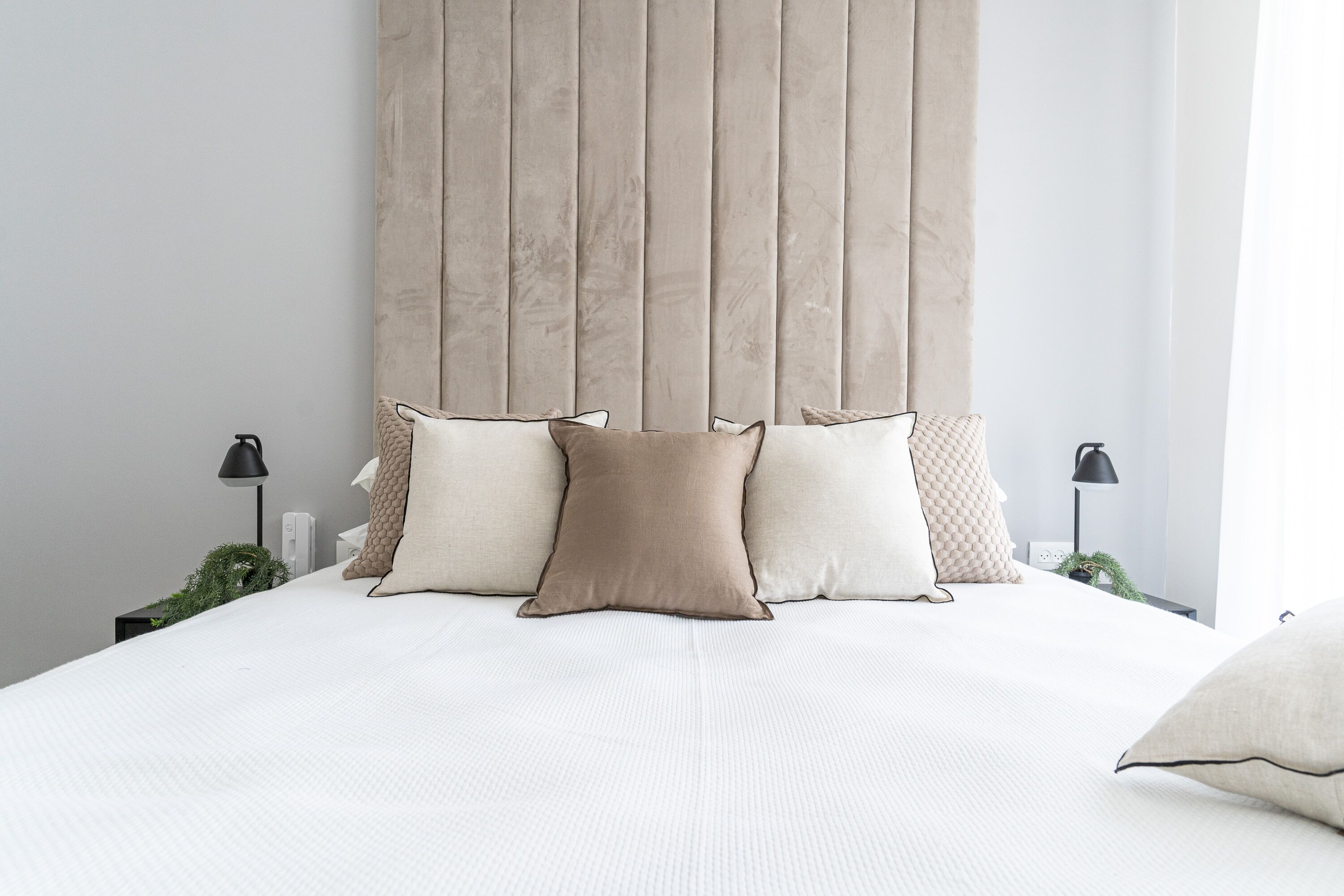 A neatly made bed with a white duvet and four pillows in a modern bedroom with a tall, textured headboard.