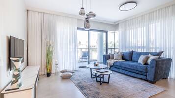 Un salon moderne avec un canapé bleu, une table basse blanche et une grande fenêtre ornée de rideaux légers.
