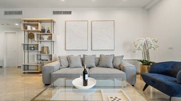 Una sala de estar moderna con un sofá gris, una mesa de centro de vidrio y una estantería.