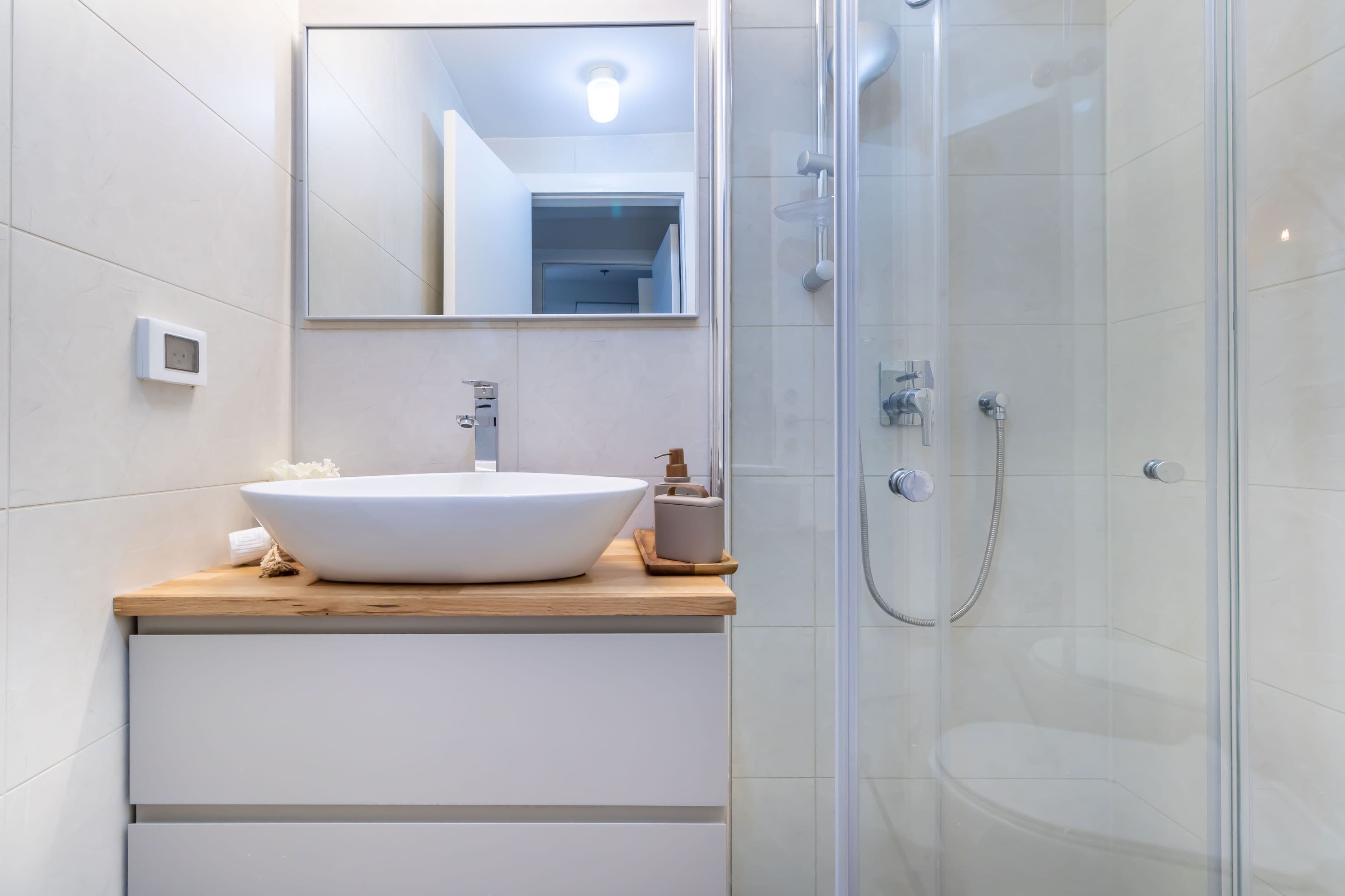 A modern bathroom with a large white sink, a mirror, and a glass-enclosed shower.