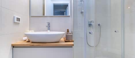 A modern bathroom with a large white sink, a mirror, and a glass-enclosed shower.