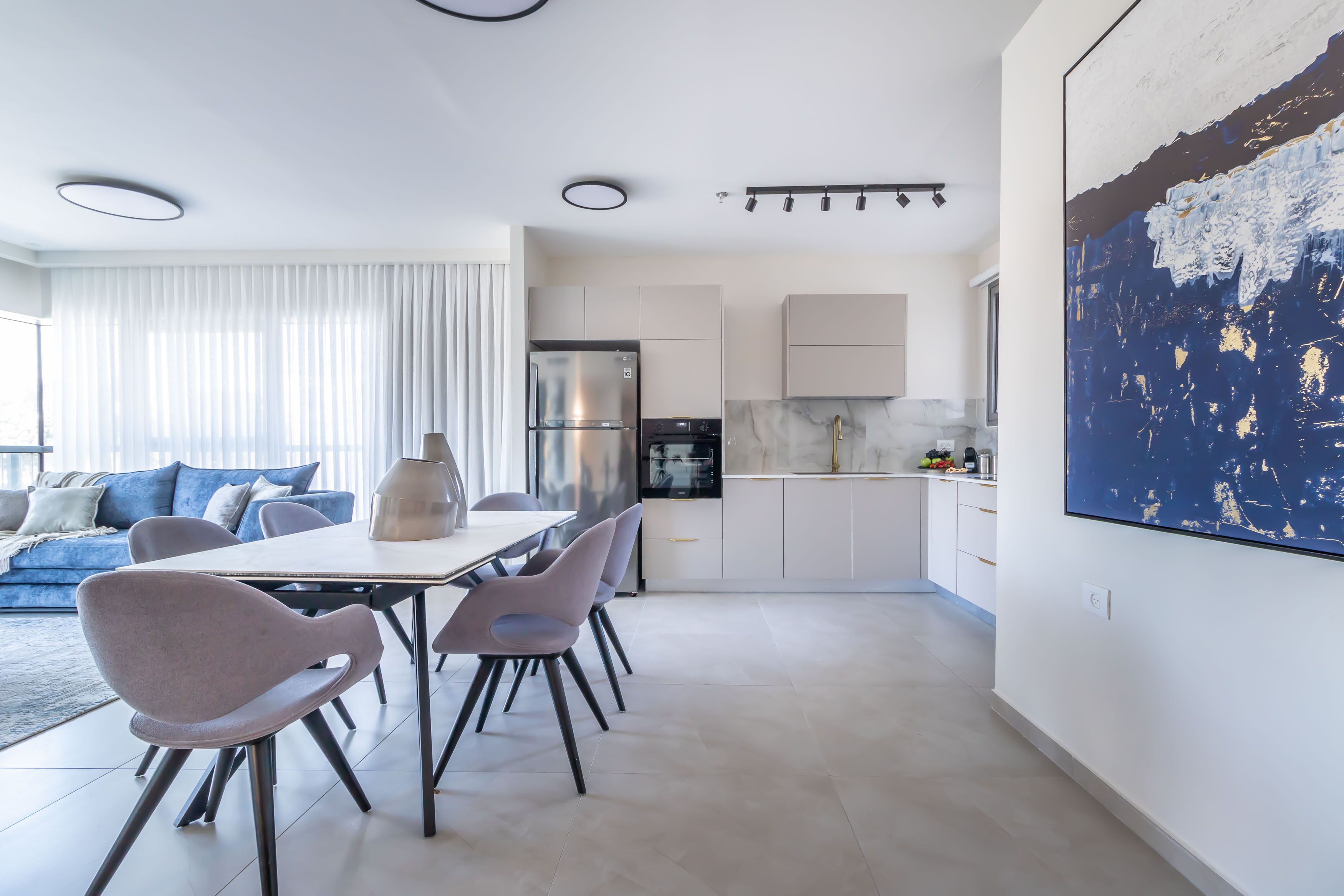 A modern living space with a dining area, kitchen, and a large abstract painting.