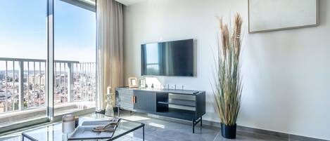 Un salon moderne doté d’une grande fenêtre, d’un téléviseur à écran plat, d’une table basse en verre et d’une console au design minimaliste.