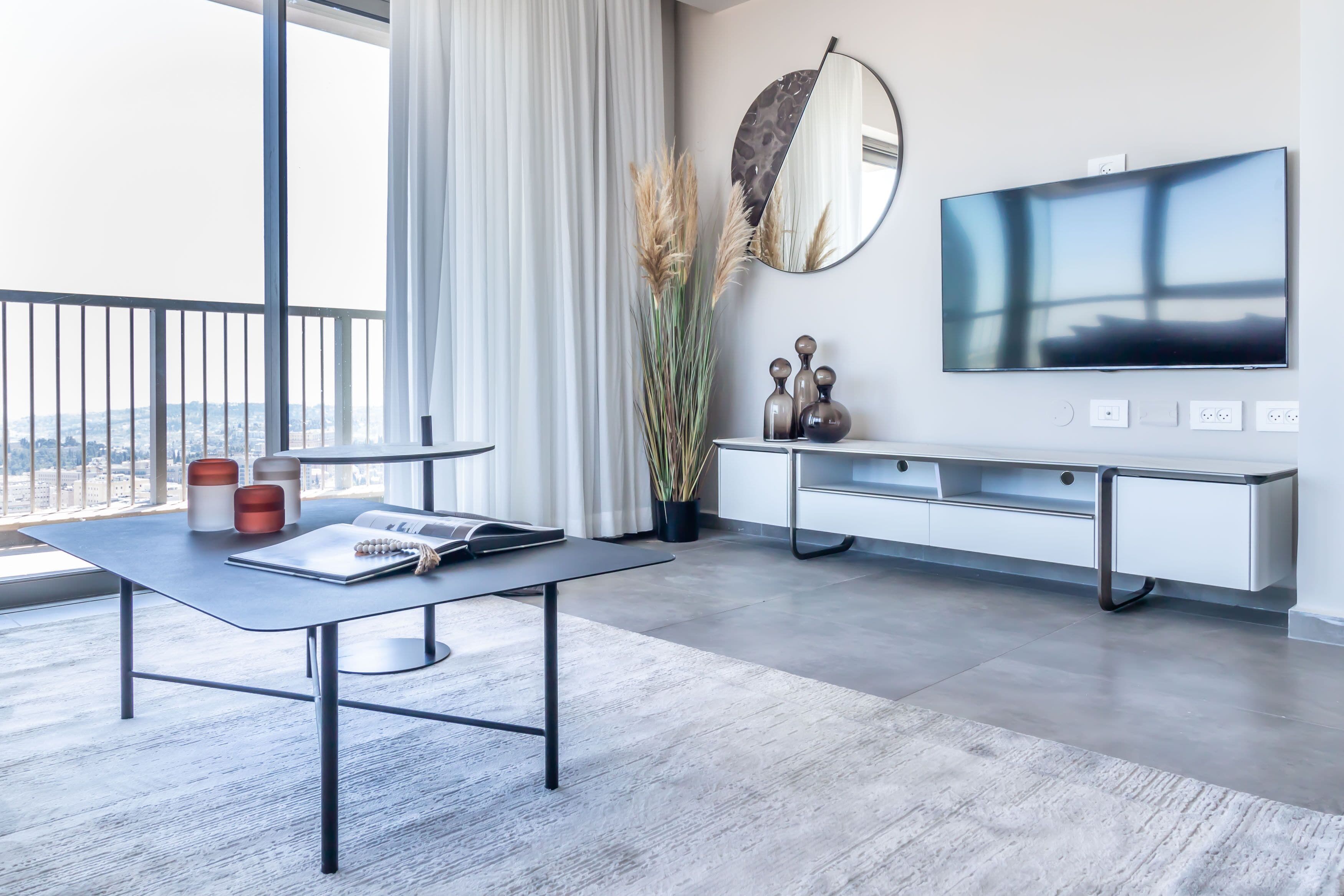 A modern living room with a large window, a flat-screen TV, a white console table, and a grey sofa.