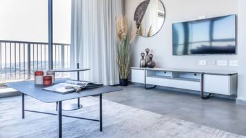 A modern living room with a large window, a flat-screen TV, a white console table, and a grey sofa.