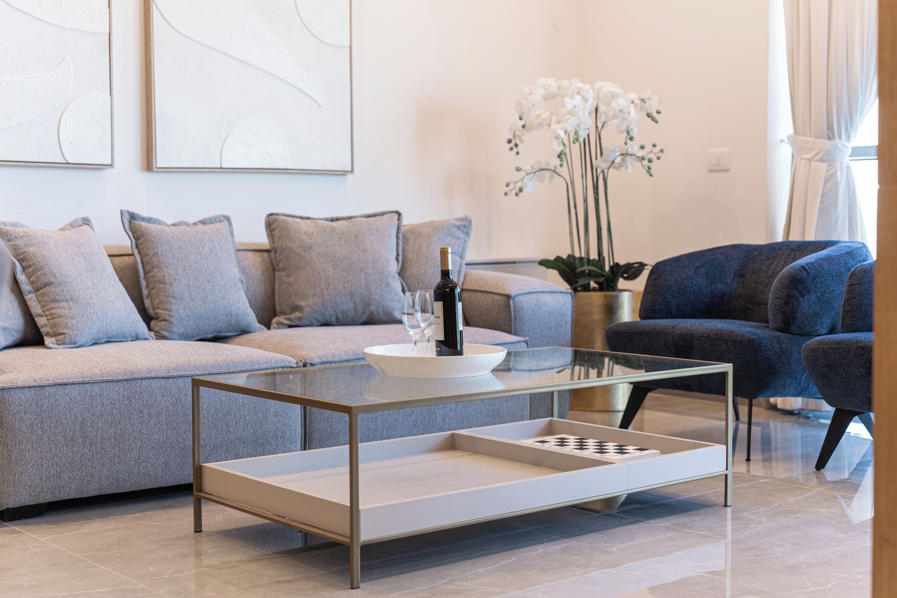 A modern living room with a glass coffee table, a sofa, and a blue armchair.