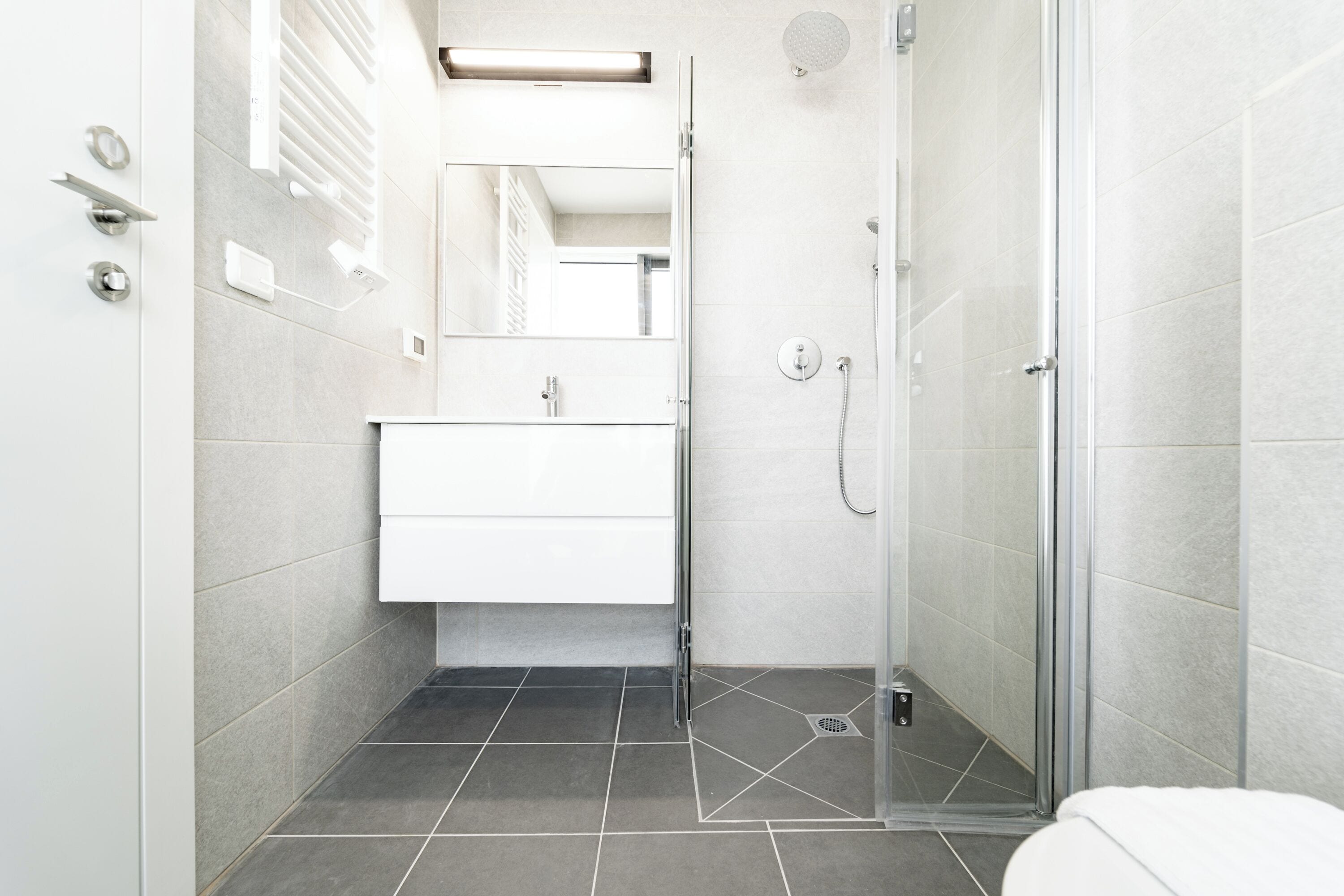 A modern bathroom with a glass shower enclosure, a white sink, and a mirror above the vanity.