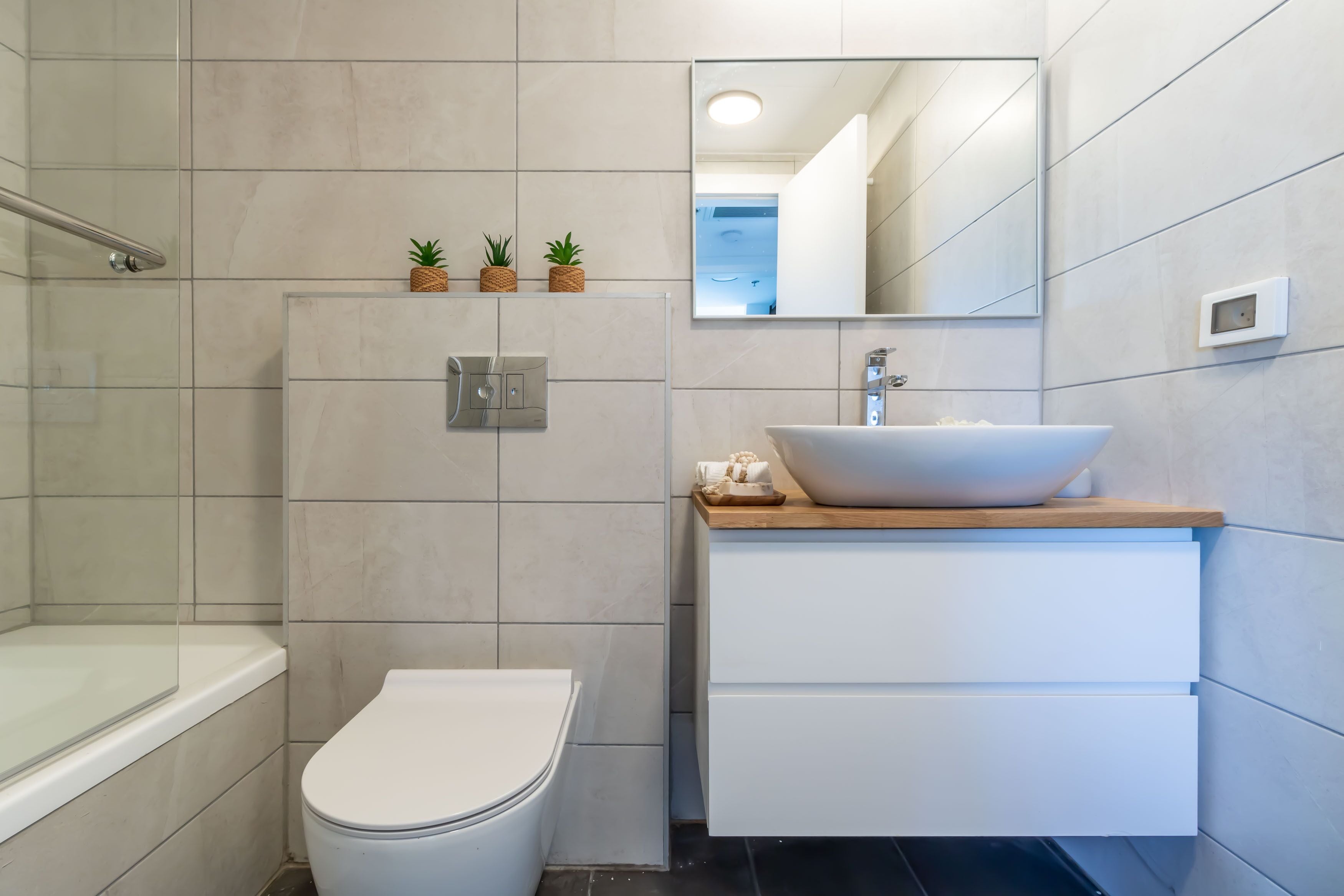 A modern bathroom with a white toilet, a wooden vanity with a large sink, and a mirror above the vanity.