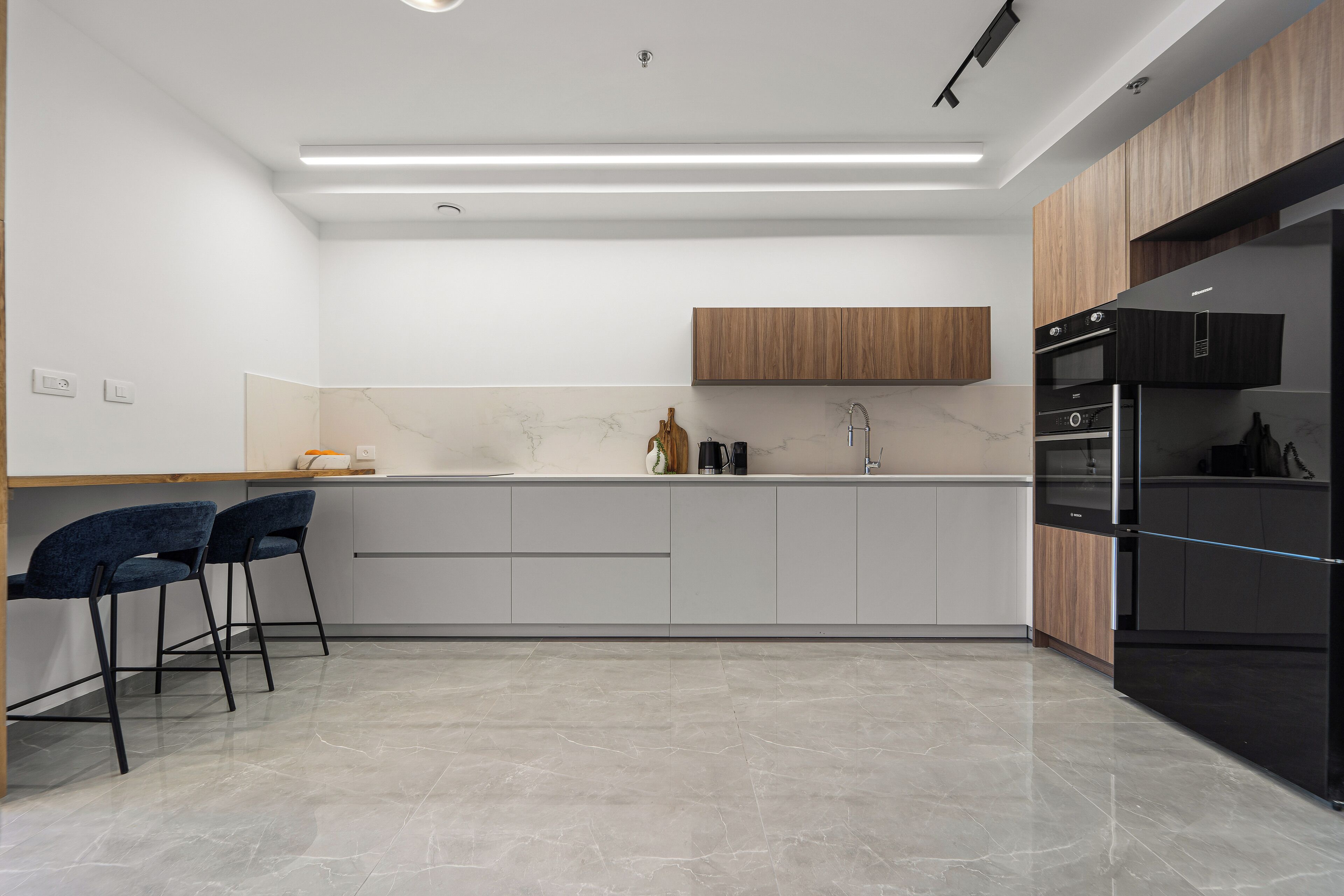 A modern kitchen with a marble countertop, wooden cabinets, and a black refrigerator.