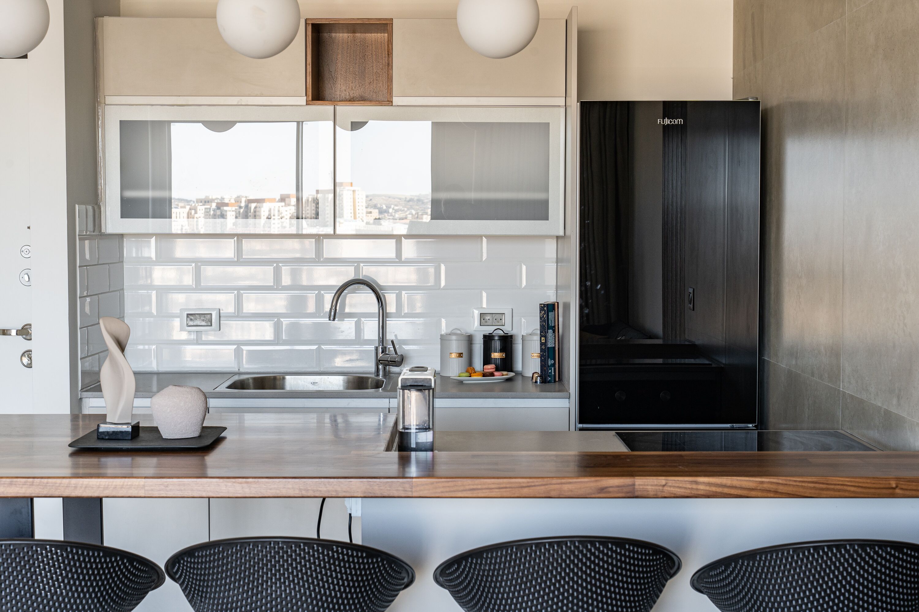 A modern kitchen with a stainless steel refrigerator, a large window, and a bar area with chairs.