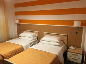 A hotel room with two beds, a nightstand with a phone, and a wall-mounted light fixture. - Twelve Hotel (Moncalieri)