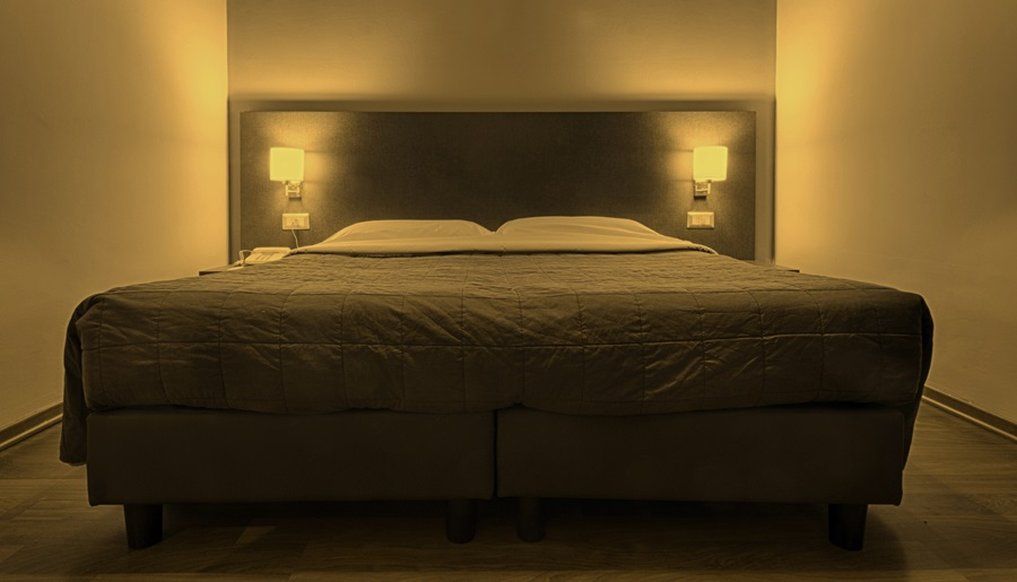 A single bed with a headboard, two bedside lamps, and a wooden floor.