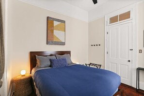 A neatly arranged bedroom with a large bed, a bedside lamp, a framed artwork on the wall, and a white door.