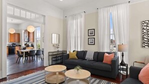 A modern living room with a dark sofa, two round coffee tables, and a striped rug. There is a dining area with a table and chairs visible through an open doorway. - Fab Marigny | 2BD Flat | Close to French Quarter (New Orleans)
