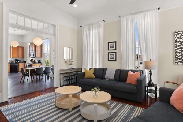 A modern living room with a dark sofa, two round coffee tables, and a striped rug. There is a dining area with a table and chairs visible through an open doorway.