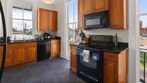 A kitchen with wooden cabinets, a black stove, and a microwave. - Fab Marigny | 2BD Flat | Close to French Quarter (New Orleans)
