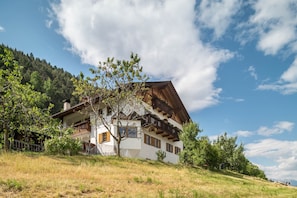 A traditional chalet with a sloped roof, wooden balconies, and a view of a forested hillside.