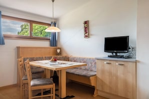 A room with a wooden table, bench seating, a television, and a window with curtains.