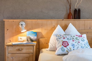 A wooden bedside table with a book, a wall-mounted light, and a power outlet.