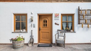 Una construcción rústica con puerta de madera, dos ventanas, un banco y una planta en maceta.