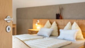 Un dormitorio con cabecera de madera, cama con ropa de cama blanca y mesita de noche con lámpara.