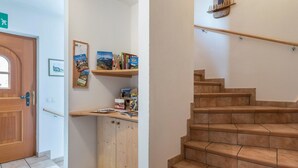Un pasillo con una puerta de madera, un tablón de anuncios con folletos de viajes, un mueble de madera y una escalera con escalones de madera.