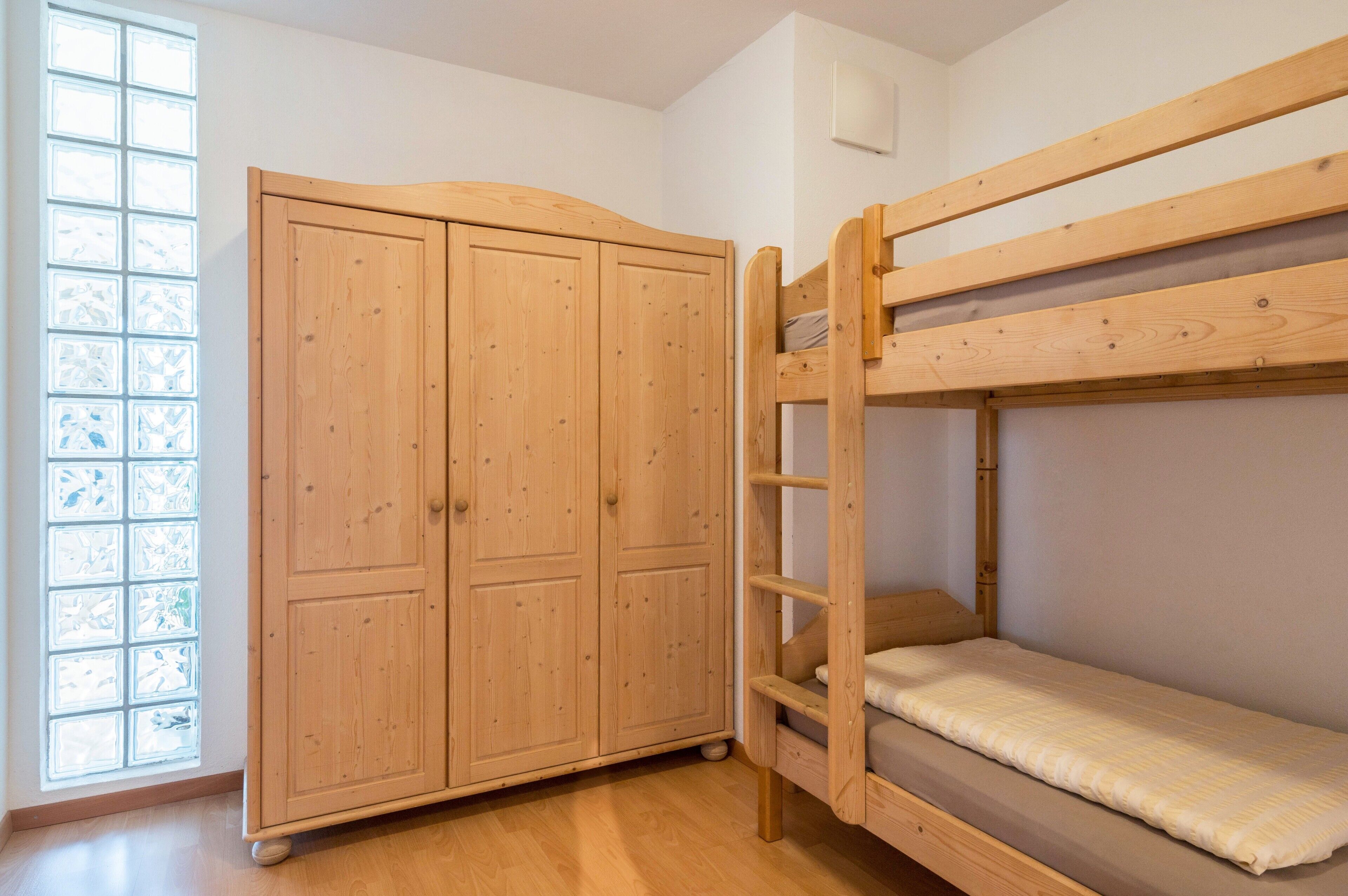 A bunk bed with a wooden headboard, a wardrobe with two doors, and a large window with a view.