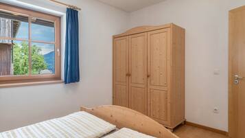 A bedroom with a wooden wardrobe, a bed, a window with a view, and a curtain.