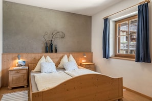 Un dormitorio con cama de madera, mesitas de noche, lámpara de pared, ventana con cortinas y vistas a un balcón.