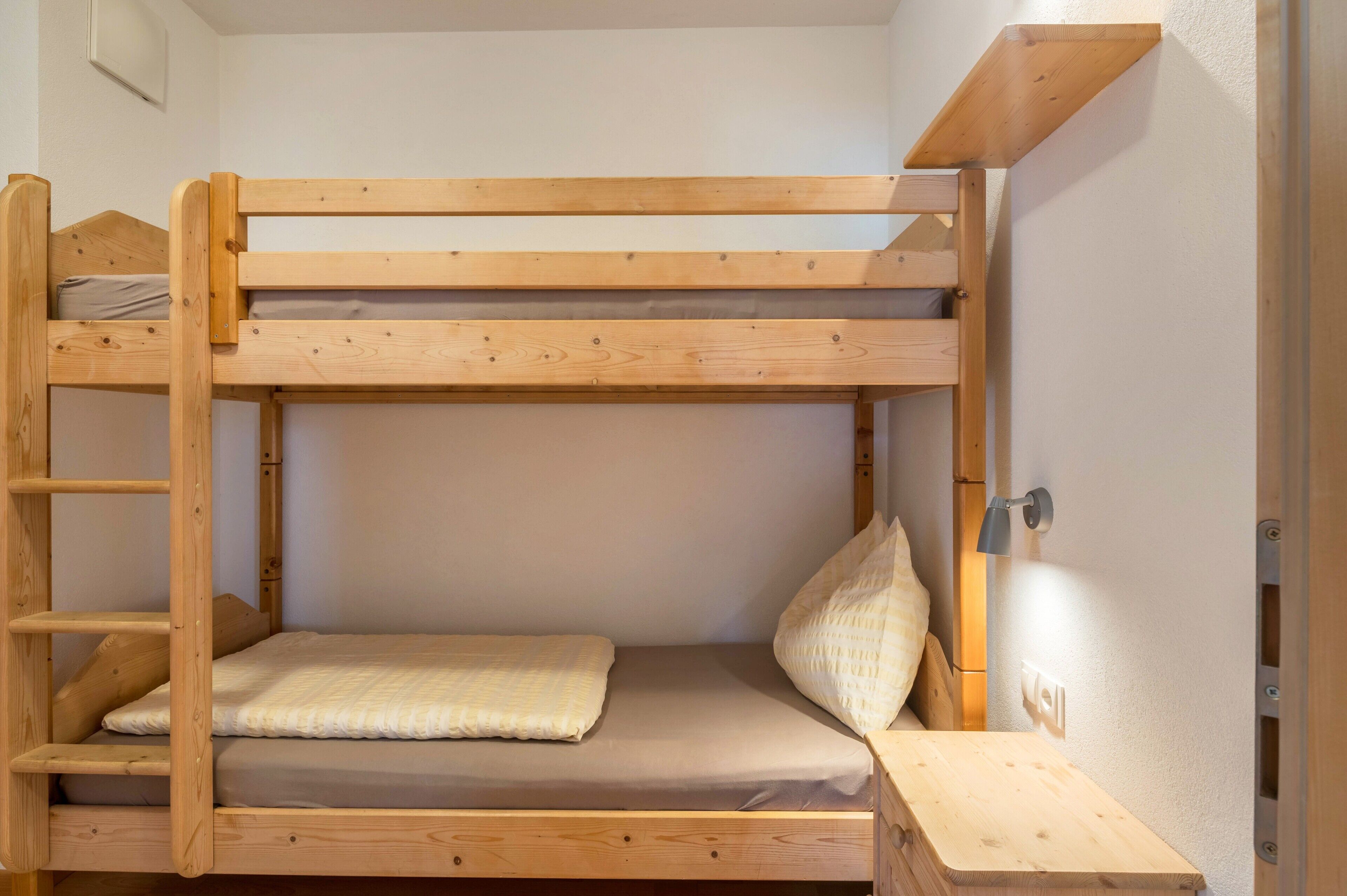 Una cama litera con escalera, una mesita de noche y una lámpara fijada a la pared.