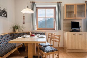 Un comedor con una mesa de madera, sillas, una banca, una ventana con cortinas, una planta en maceta y un televisor sobre un mueble de madera.