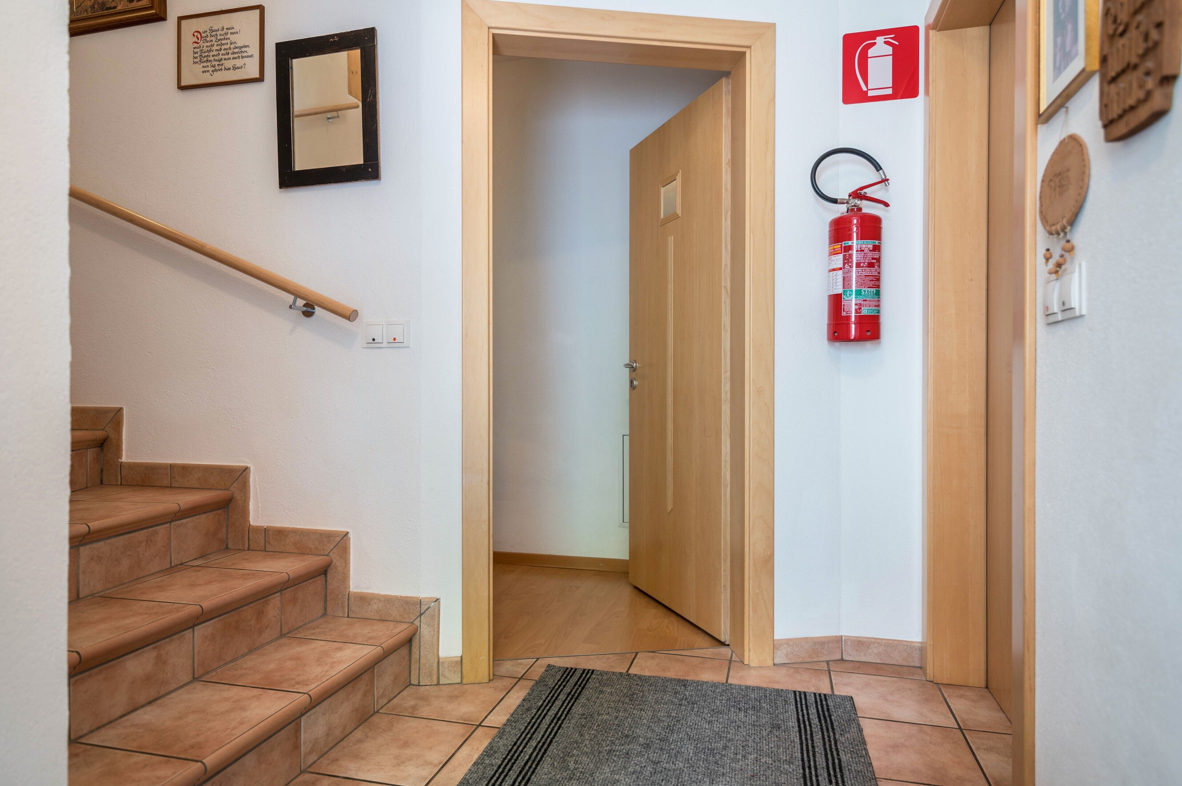 Un corridoio con una porta in legno, un estintore, uno specchio e una scala.