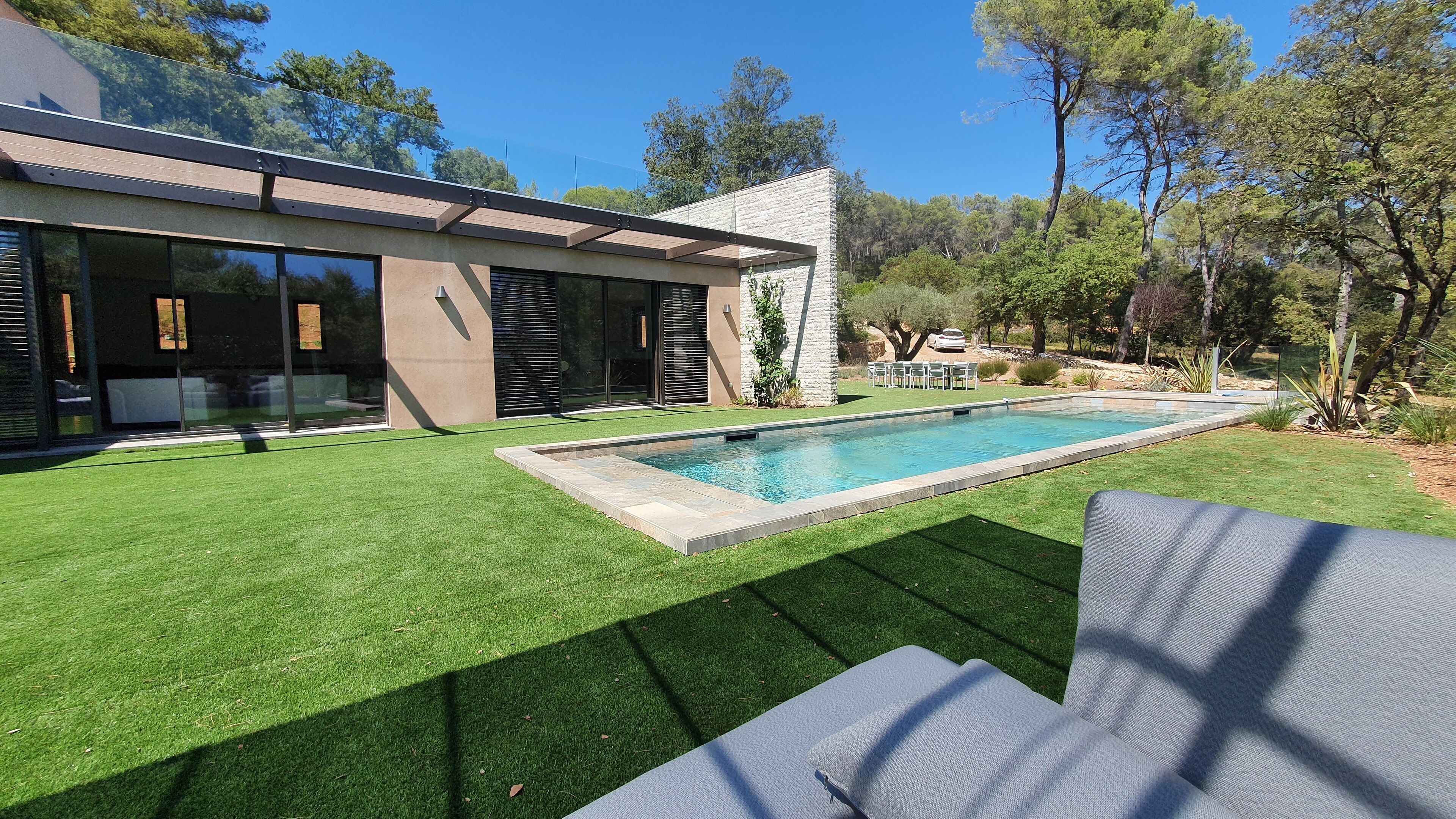 A modern house with a swimming pool, green lawn, and outdoor furniture.