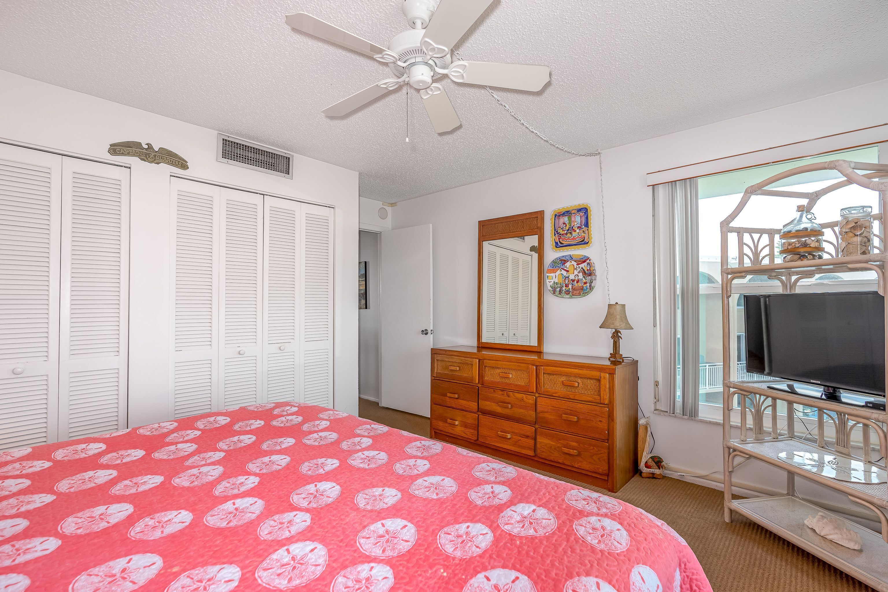 A bedroom with a bed, a dresser, a television, and a window with a view.