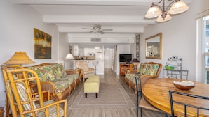 Un vaste salon meublé de meubles en osier, avec une table à manger en bois et une cuisine à l’arrière-plan.